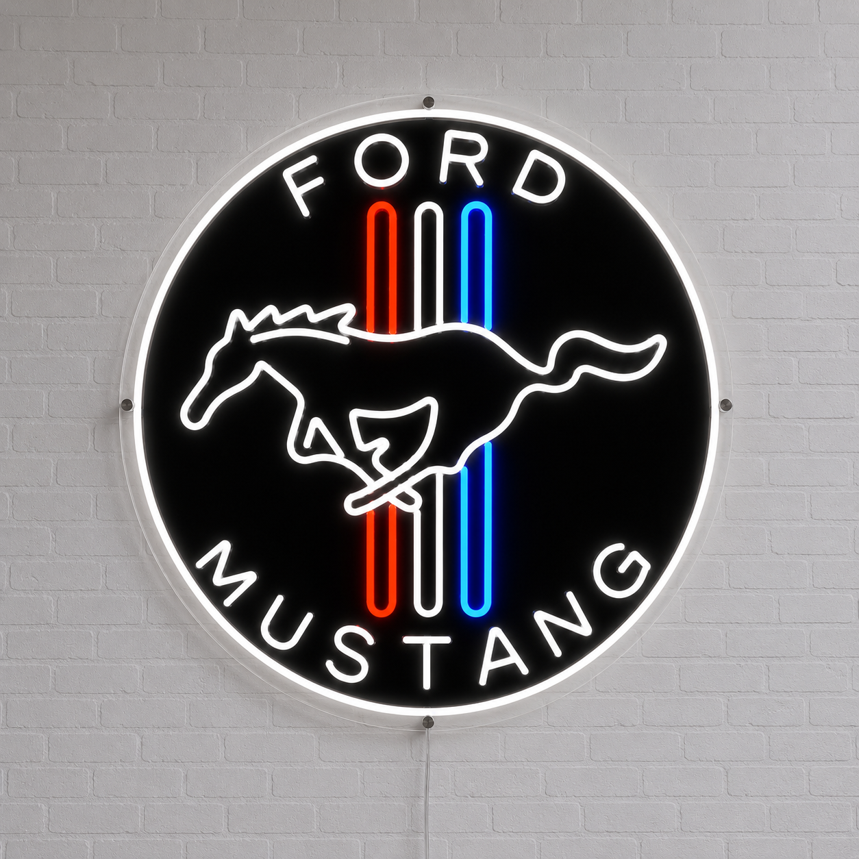 A circular Ford Mustang neon-style wall sign mounted on a white brick wall. The sign has a black background with a white running horse logo, white 'FORD' at the top and 'MUSTANG' at the bottom, and three vertical stripes in red, white, and blue.