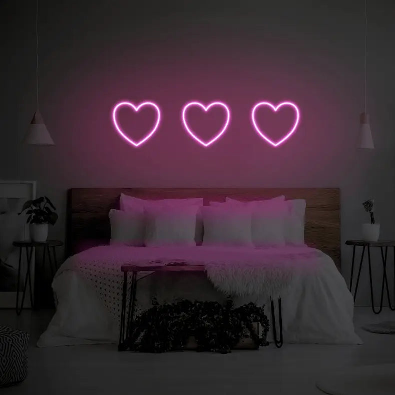 3 Hearts LED Neon Light Sign in pink, featuring three heart outlines illuminated above a bed.