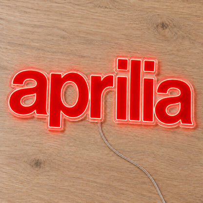 Aprilia LED Neon Sign, featuring illuminated vehicle logo on a wooden surface.