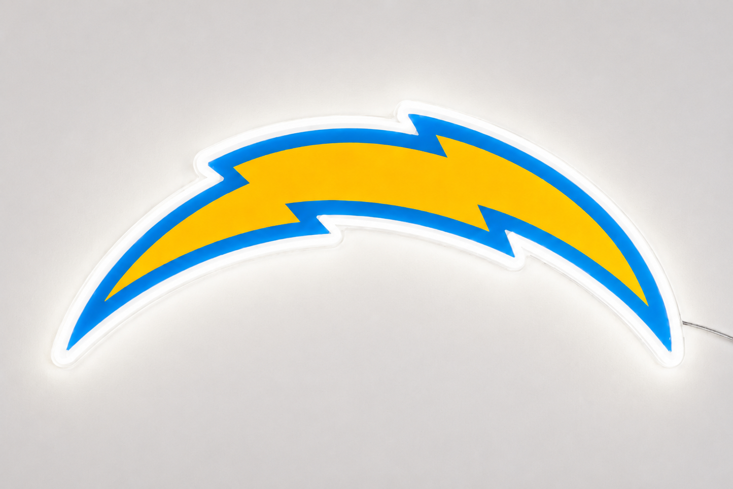 An illuminated LED neon sign of the Los Angeles Chargers lightning bolt logo, featuring a bright yellow center with a blue outline and a glowing white border, set against a neutral light gray background.