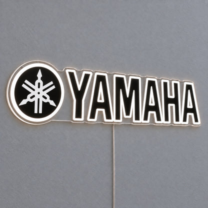 Yamaha (Black) LED Neon Sign in white, featuring Yamaha lettering beside a tuning-fork emblem on a grey wall.