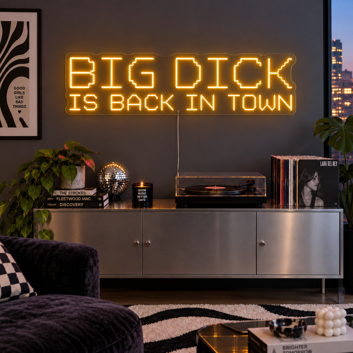 Big Dick Is Back In Town Neon Sign glowing gold above a record player and metal sideboard.