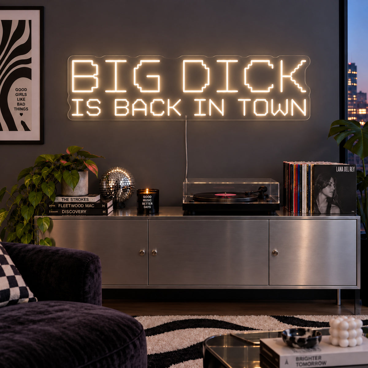 Warm White version of the Big Dick Is Back In Town Neon Sign, shown above a record player and metal sideboard.
