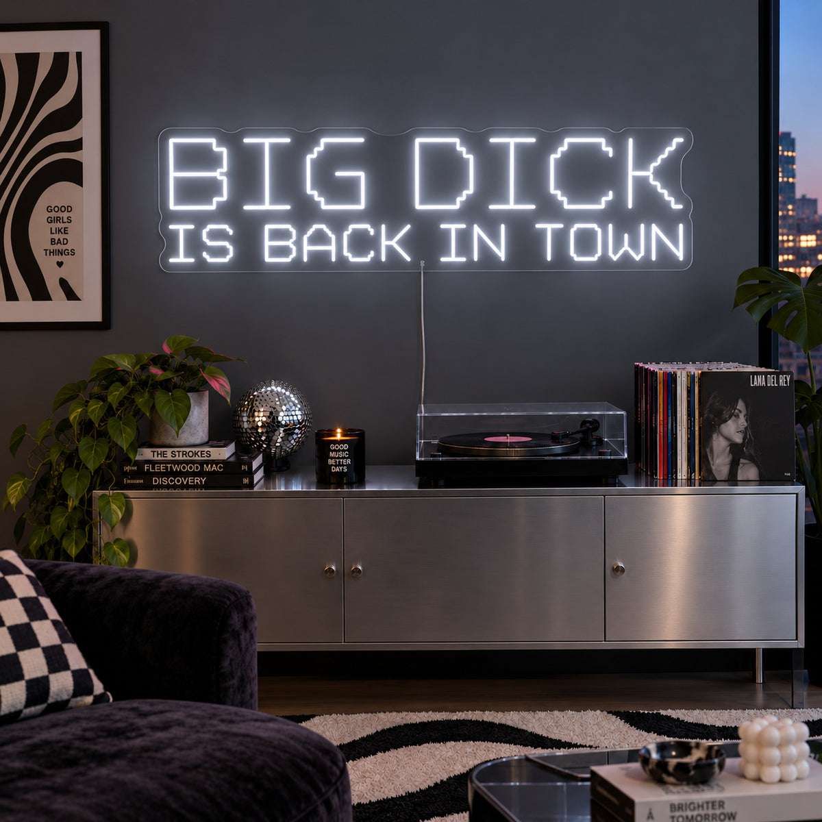 Big Dick Is Back In Town Neon Sign glowing white above a record player and metal sideboard.