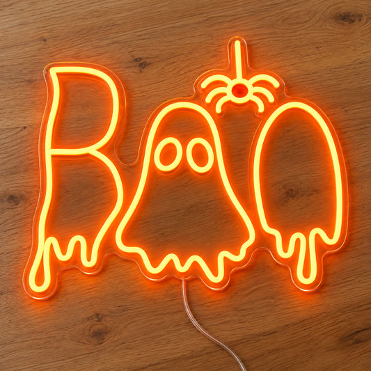 Boo Ghost and Spider Neon Sign featuring orange Boo lettering with a white ghost in the centre and a hanging orange spider, illuminated on clear acrylic lying on a natural oak wooden surface.
