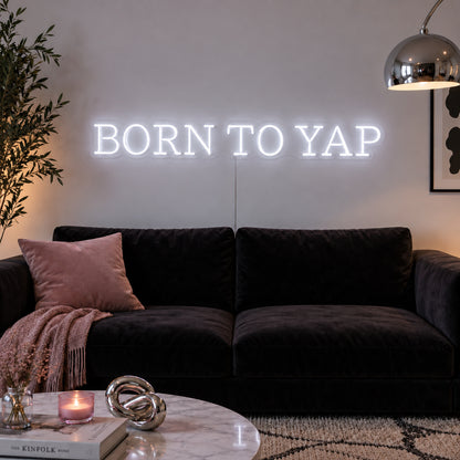 Born To Yap Neon Sign, RGB colour-changing option shown in white above a dark sofa and glass coffee table.