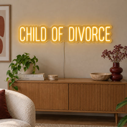 Child Of Divorce Neon Sign glowing gold above a wooden sideboard with plants.