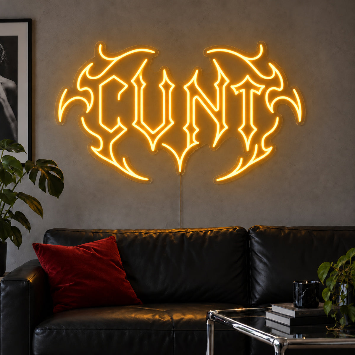 Cunt Neon Sign glowing gold in a tribal design above a black leather sofa.