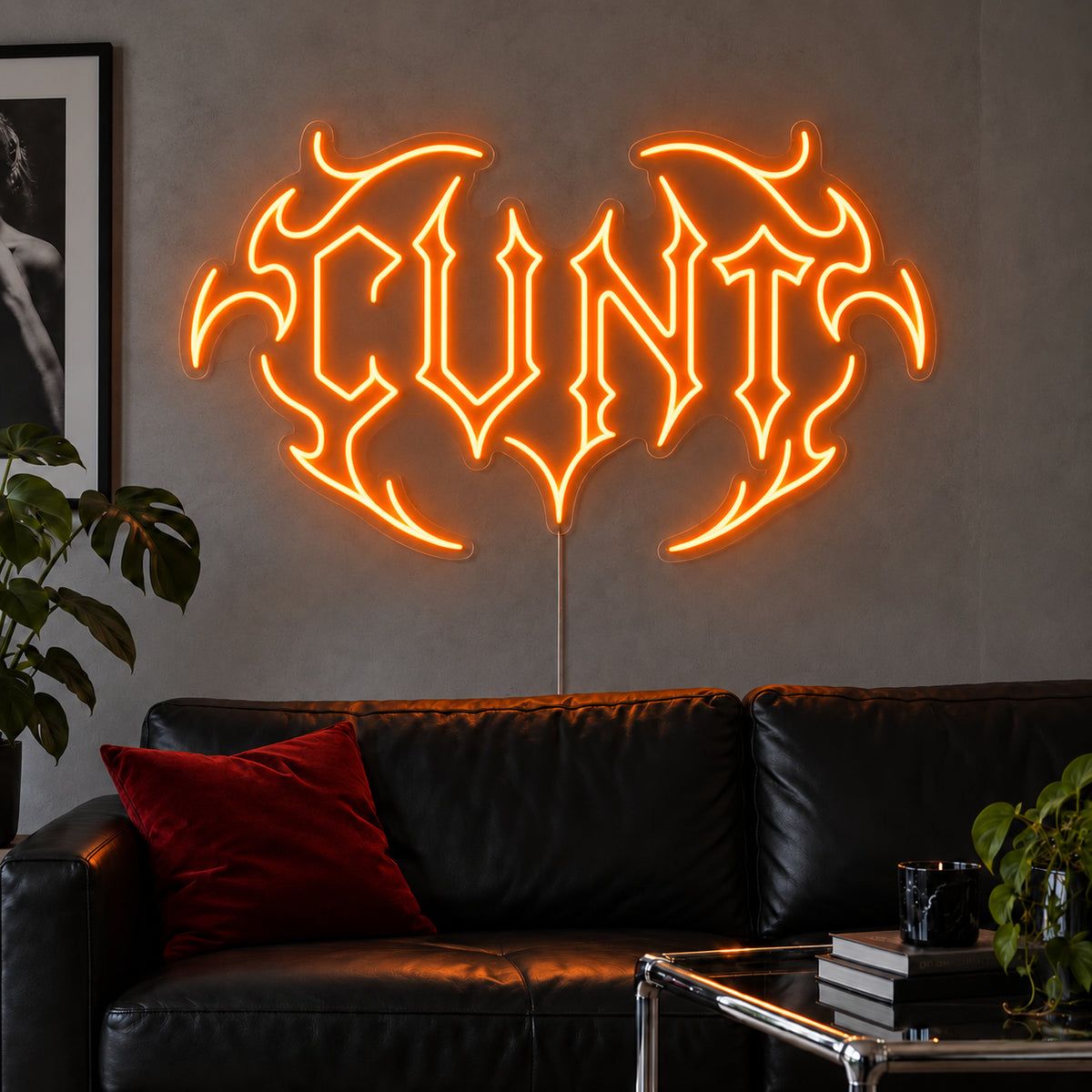 Orange version of the Cunt Neon Sign, shown in a tribal design above a black leather sofa.