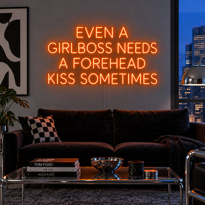 Orange version of the Even A Girlboss Needs A Forehead Kiss Sometimes Neon Sign, shown above a dark sofa and mirrored coffee table.