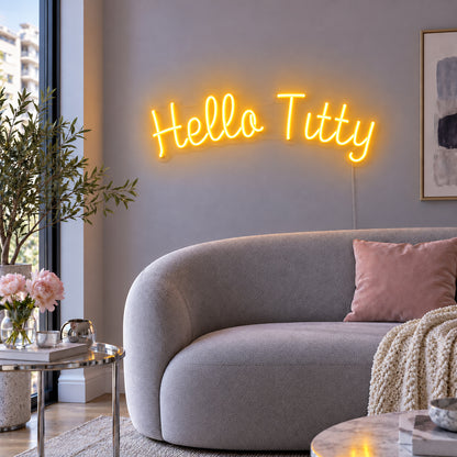 Hello Titty Neon Sign glowing gold above a curved grey sofa.