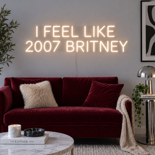 Warm White version of the I Feel Like 2007 Britney Neon Sign, shown above a burgundy sofa.