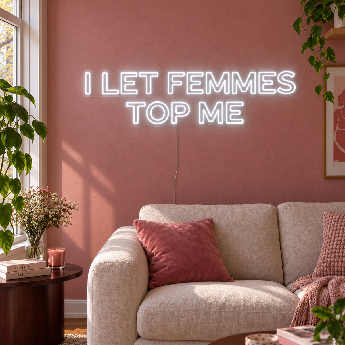 I Let Femmes Top Me Neon Sign glowing white in outlined lettering above a cream chair.
