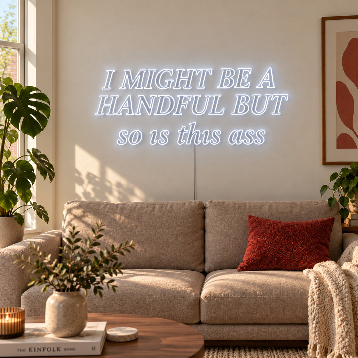 I Might Be A Handful But So Is This Ass Neon Sign glowing white in compact lettering above a cream sofa.