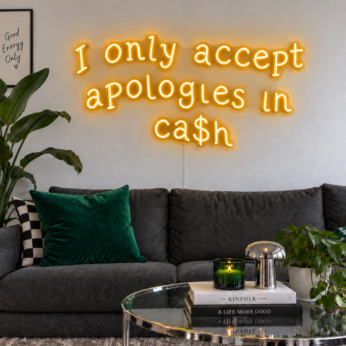 I Only Accept Apologies In Ca$h Neon Sign glowing gold above a charcoal sofa with green cushions.