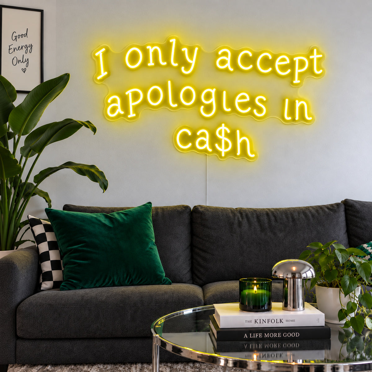 I Only Accept Apologies In Ca$h Neon Sign with yellow lighting, displayed above a charcoal sofa with green cushions.