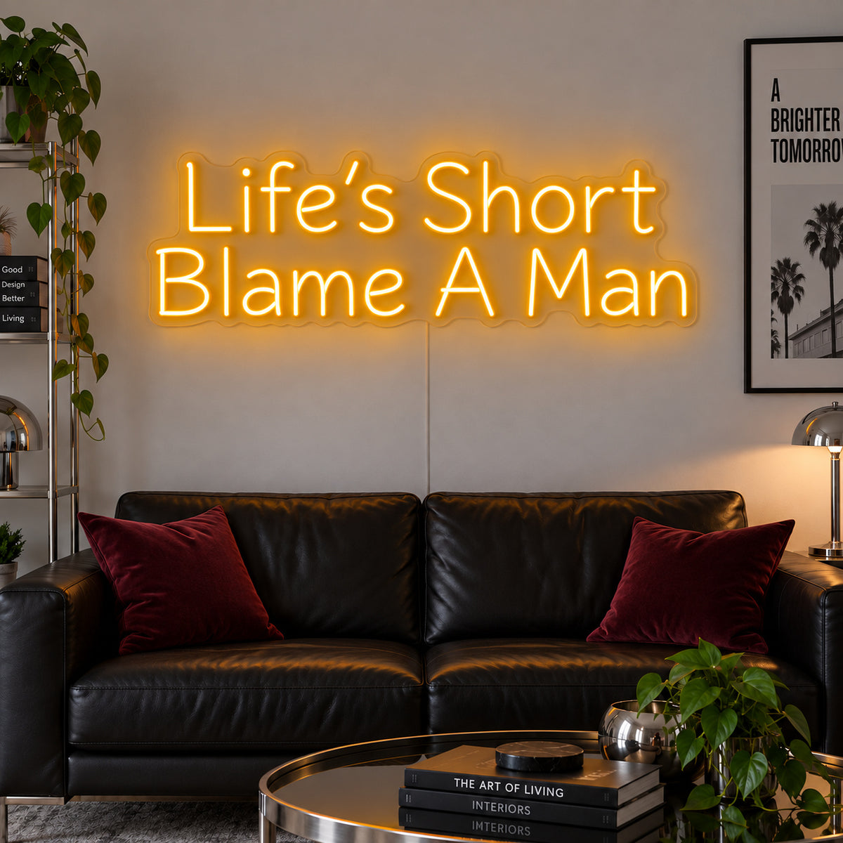 Life's Short Blame A Man Neon Sign glowing gold above a black leather sofa.