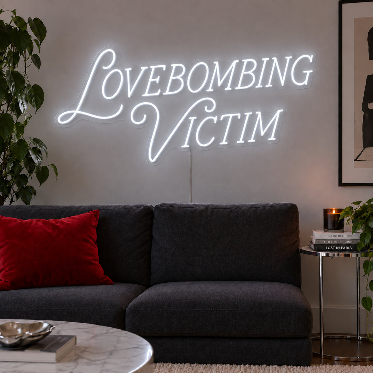 Lovebombing Victim Neon Sign glowing white above a dark sofa with red cushions.