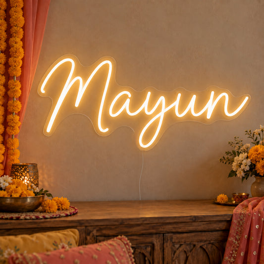 Mayun Neon Sign on clear cut-to-shape acrylic, illuminated on a wall in a styled celebration setting