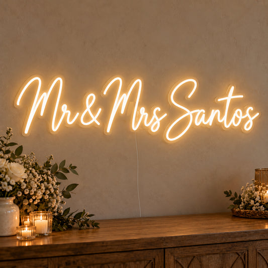 Personalised Mr & Mrs Surname Neon Sign on clear cut-to-shape acrylic, illuminated on a wall in a styled celebration setting; sample personalised wording shown