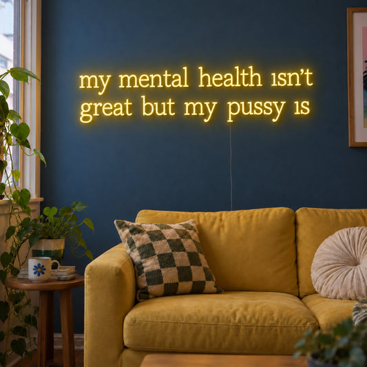 My Mental Health Isn't Great But My Pussy Is Neon Sign with warm yellow lettering arranged in two lines on transparent acrylic, displayed on a living room wall