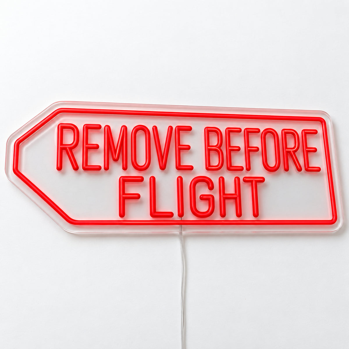 Remove Before Flight Neon Sign, featuring Remove Before Flight lettering inspired by aviation safety tags, on a single clear acrylic backing displayed on a white surface.